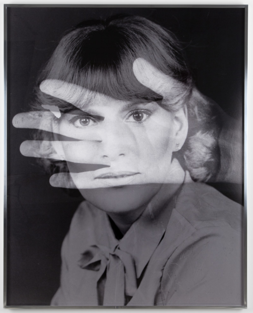 A black and white image of a light-skinned young woman with bangs staring at the camera. The image of a spread open hand is superimposed over her face.