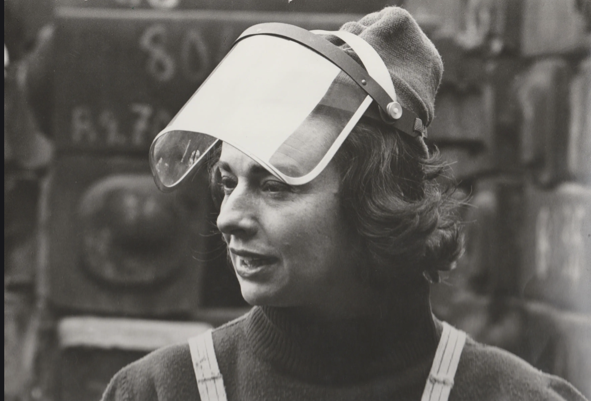 A black and white image of a light skinned woman with shoulder-length hair, a plexi-glass visor over her face.